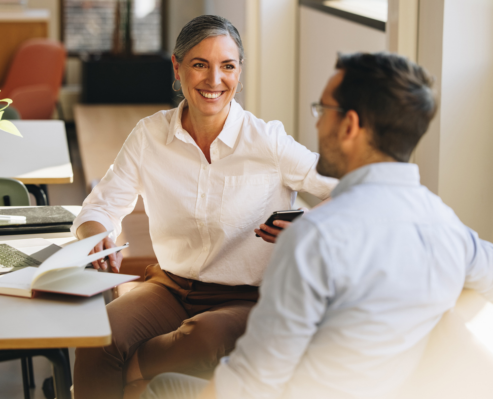 A woman in a white shirt discussing plans with a man in an office setting.