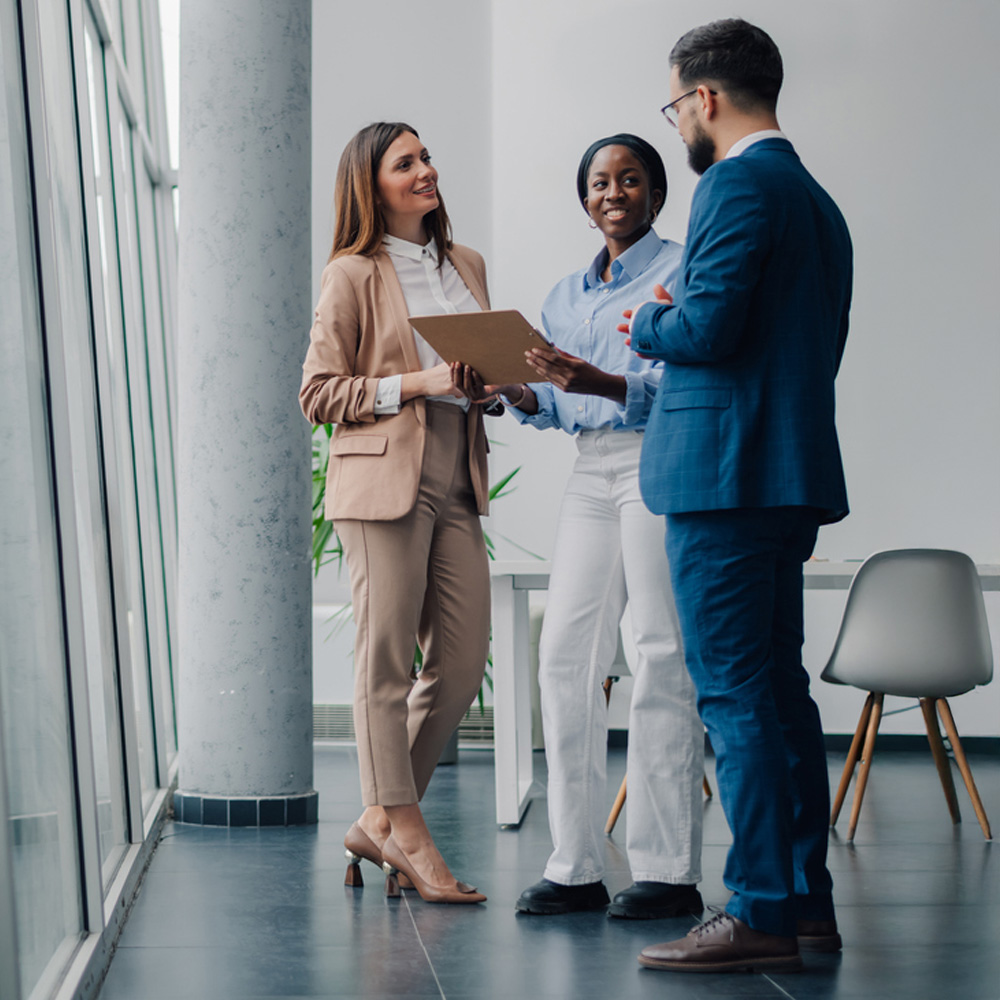 Three professionals discussing a document in a modern office hallway.